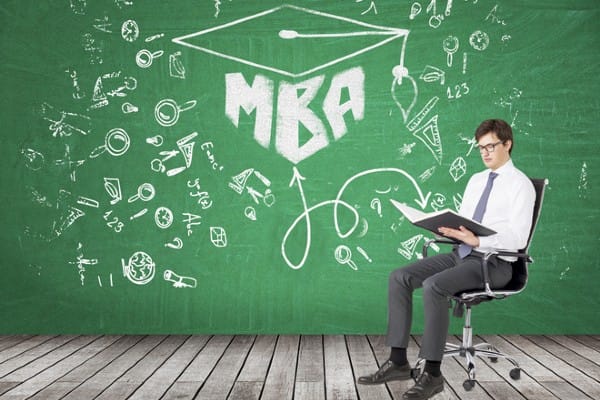 A man sits in front of a blackboard with “MBA” written on it.