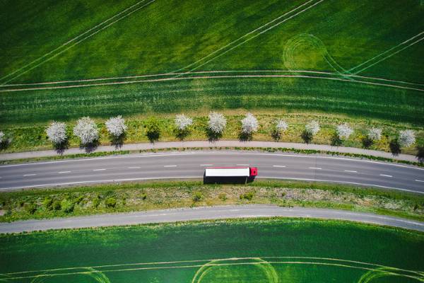 Drone shot directly above a truck moving along a single road, surrounded by green fields - supply chain sustainability concept